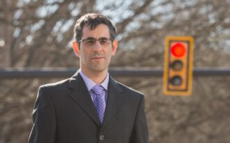 A man in a suit stands outside with a stop light behind him.