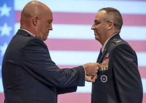 An Air Force airman in dress blues reaches out to pin an award on the uniform of another airman