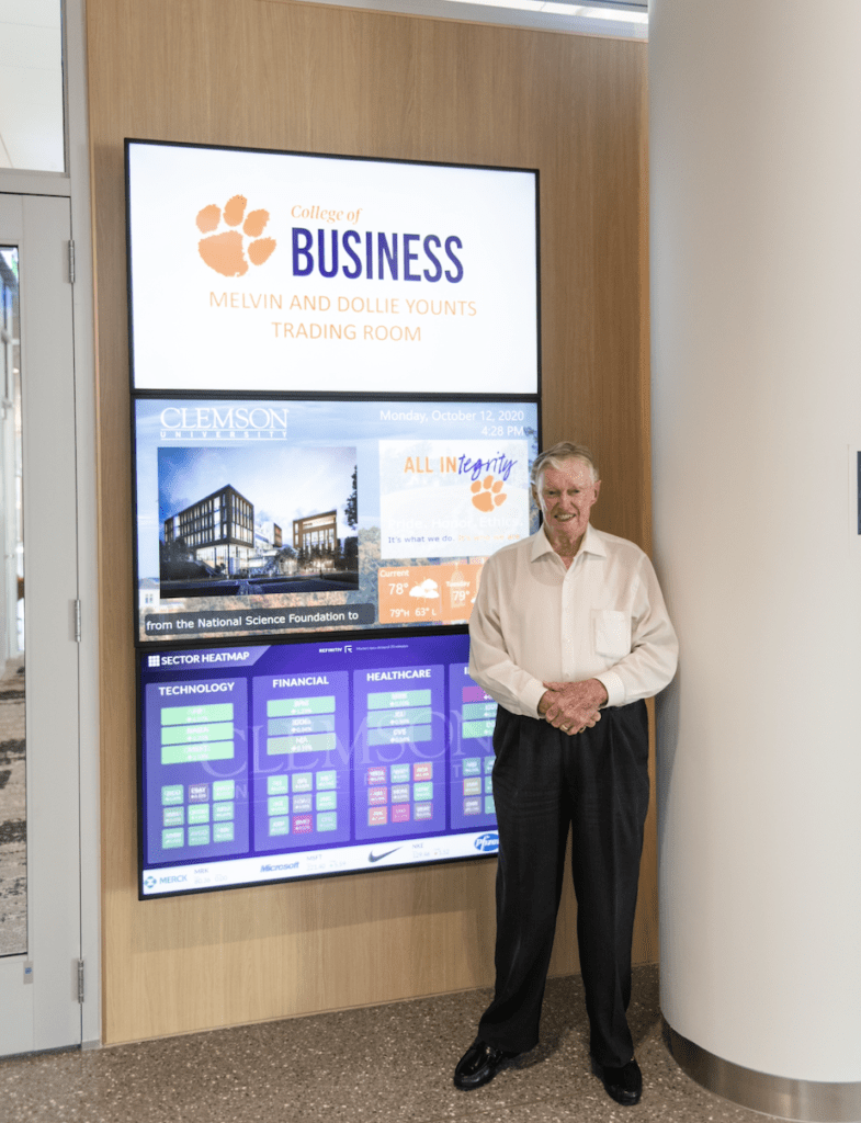 Younts in CoB building standing outside training room in front of three large TV screens with CoB logo on it.