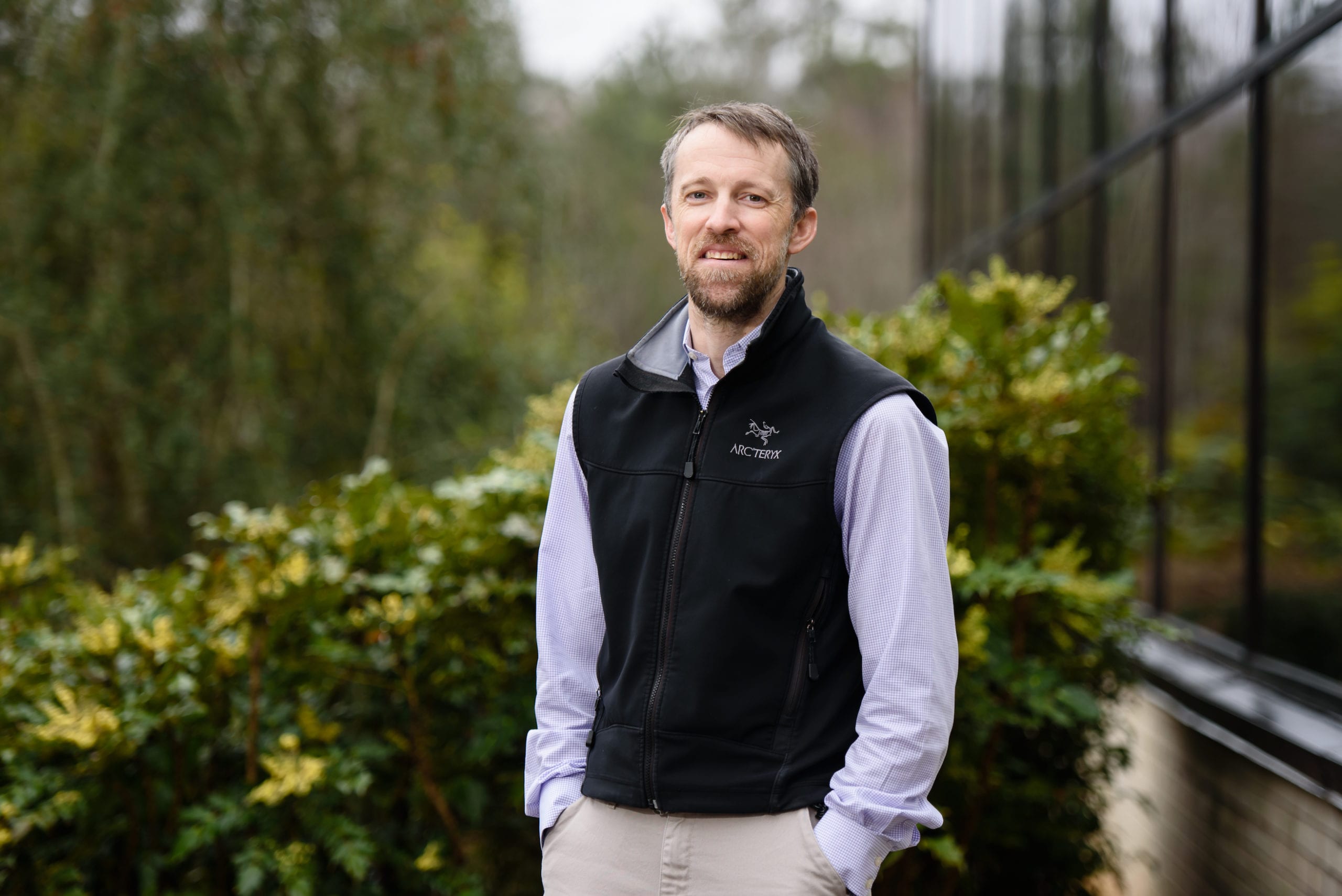 Alex Pullen standing outside a glass building surrounded by natural foliage.