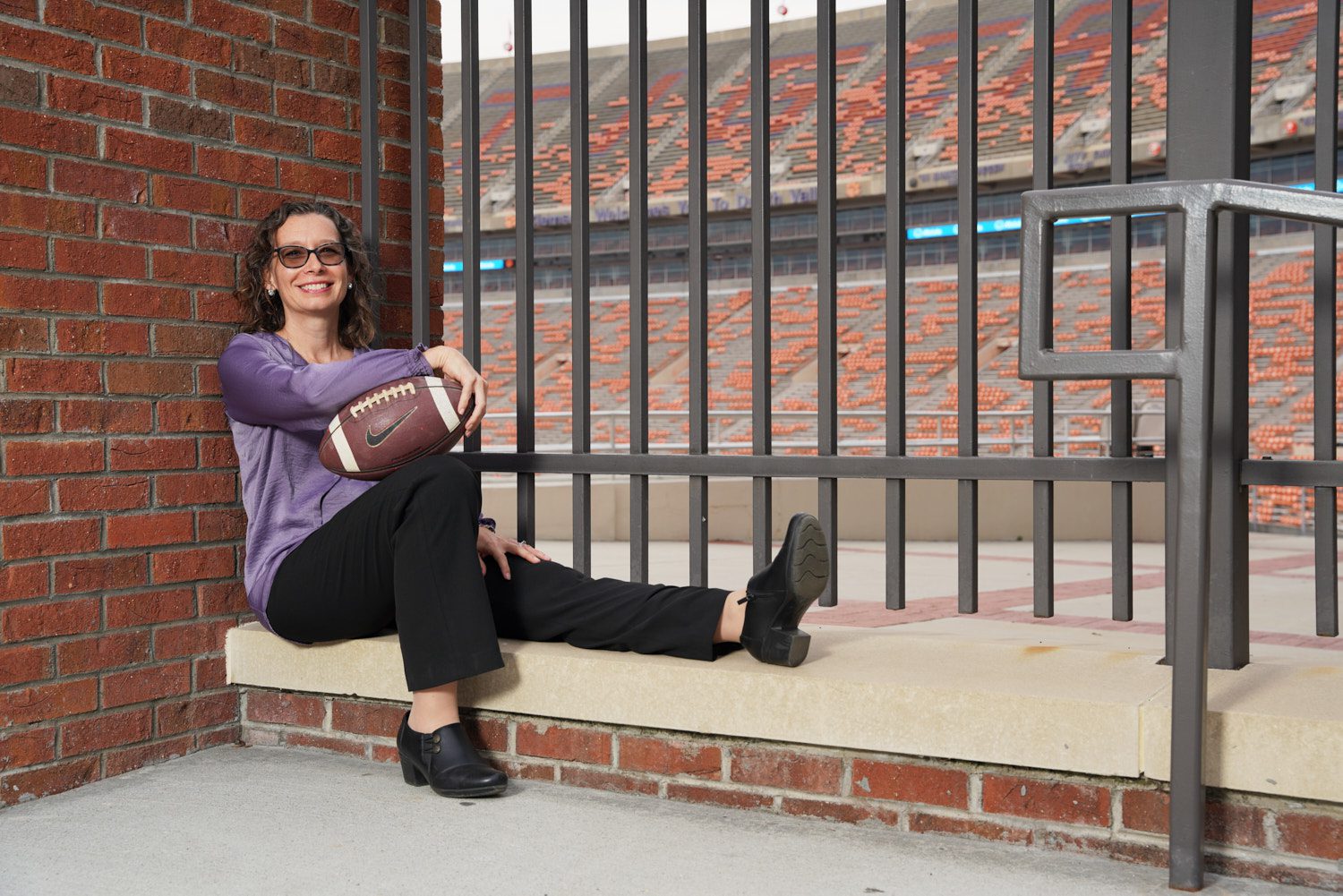 Woman holding a football sitting at a gate at Memorial Stadium