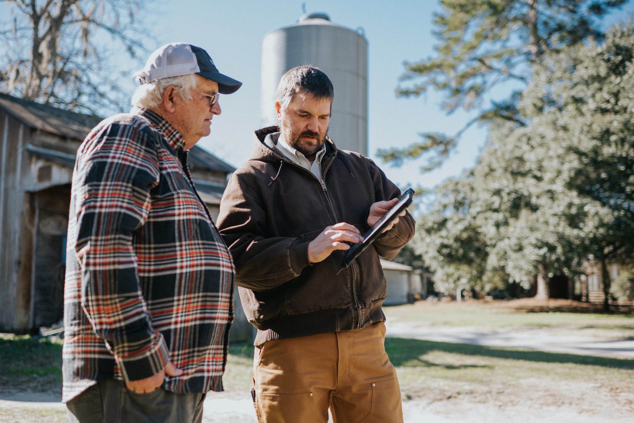 Bamberg County farmer Richard Rentz and Clemson precision agriculture engineer Kendall Kirk work with a tablet in front of a grain silo.