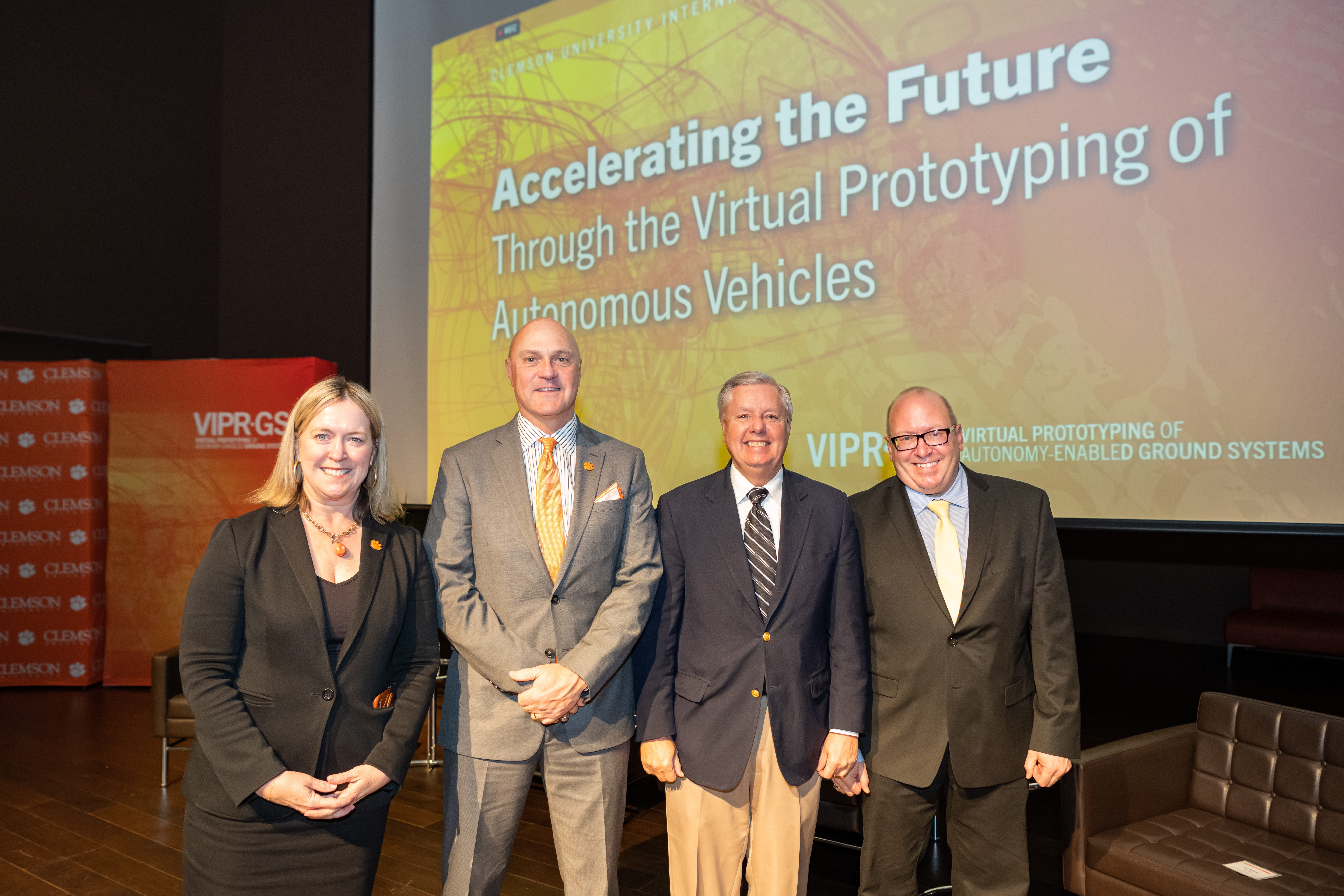 A woman and three men stand in front of a giant screen that reads Accelerating the Future Through the Virtual Prototyping of Autonomous Vehicles. This is for the Clemson Army Partnership and includes Angie Leidinger, President Jim Clements, U.S. Senator Lindsay Graham, U.S. Army Chief Scientist David Gorsich