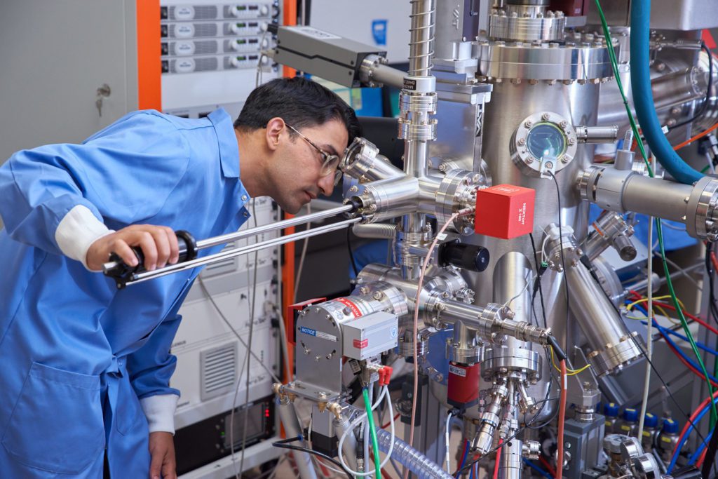 man wearing blue lab coat looks at a piece of physics lab equipment