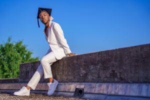 Man wearing white suit and graduation cap sitting on a concrete wall