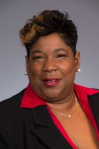 headshot of a Black woman (Corliss Outley) wearing a red blouse and black jacket
