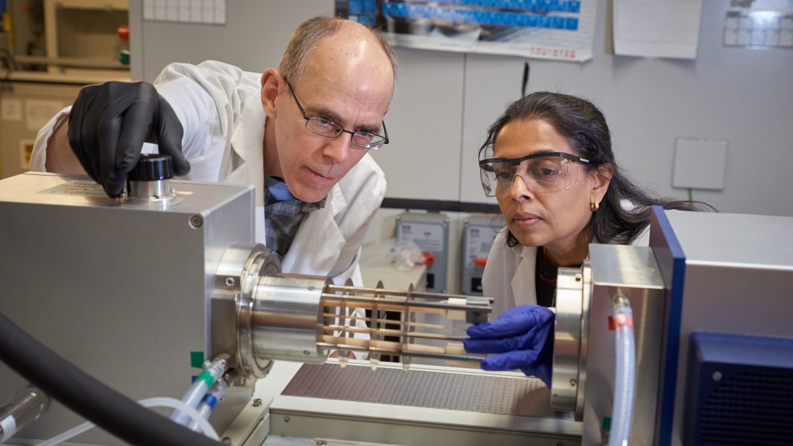Man and woman wearing lab coats are looking at a machine in the Clemson Nanomaterials Institute.
