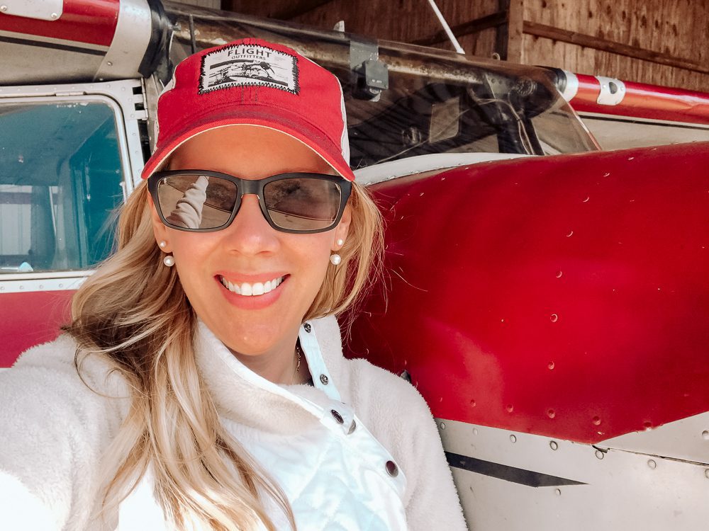 A woman wearing a red hat and sunglasses standing in front of an airplane