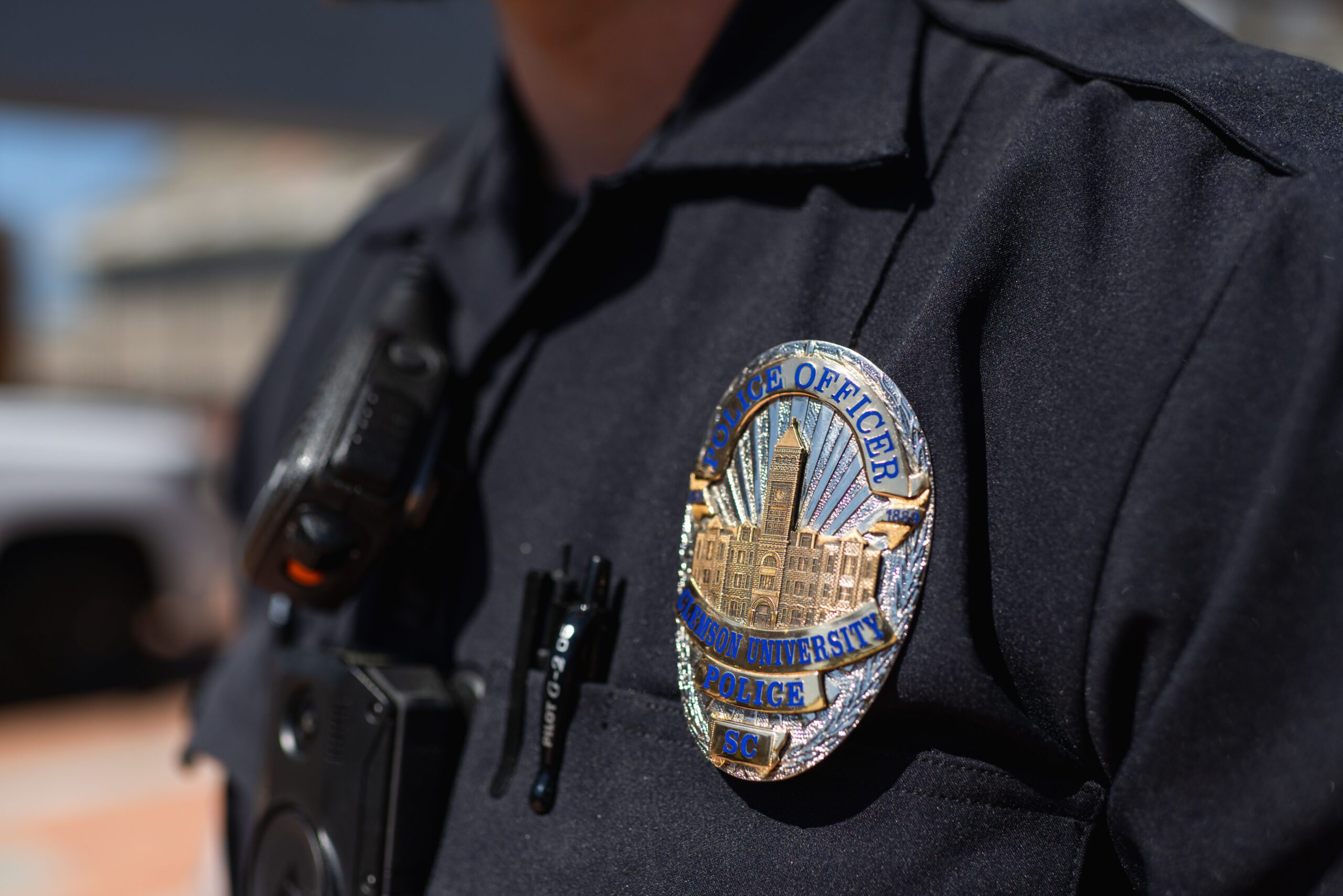 A close-up of a silver Clemson University Police Department badge on an officer's black uniform.