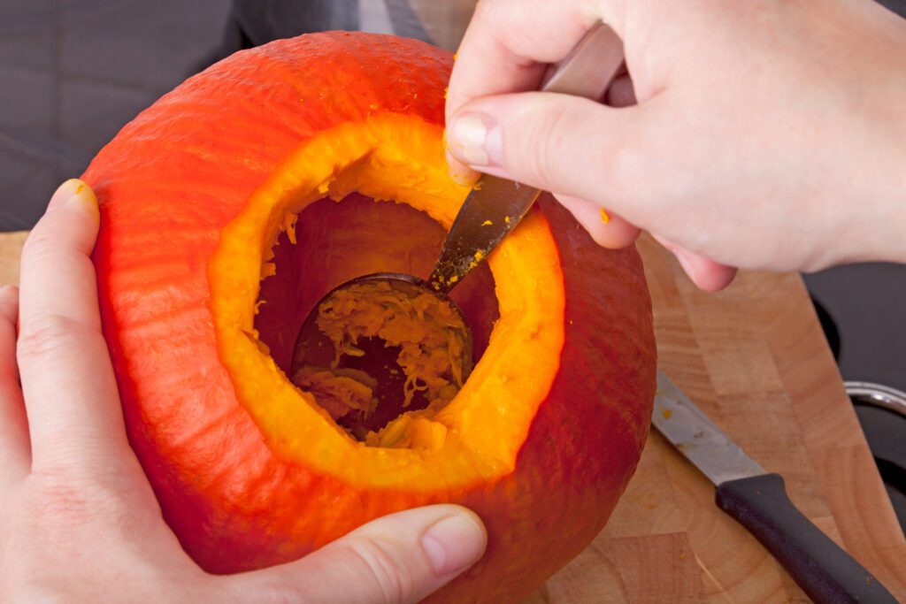 Pumpkin that is being scraped on the inside by a knife.