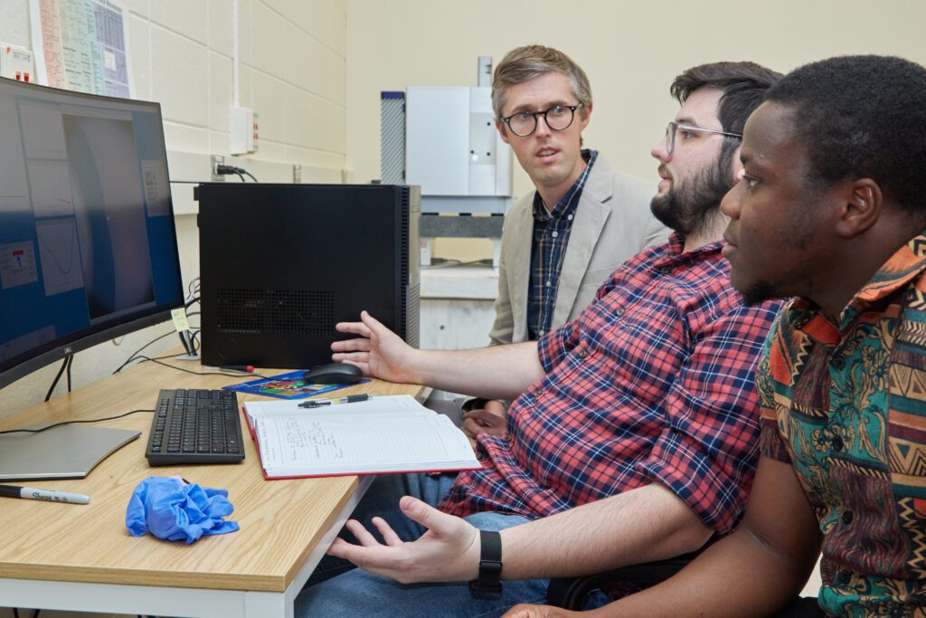 Three men, including Department of Chemistry Assistant Professor David Jacobson (left with suit jacket) talk about research that could help find a therapeutic for diabetes insidious, a rare disease.