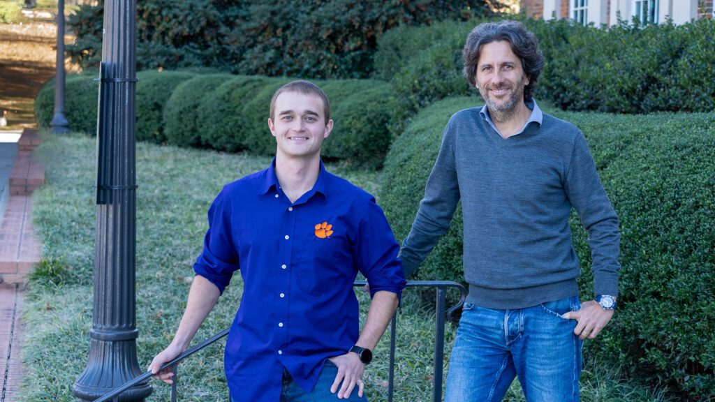 Two men standing in front of some bushes.