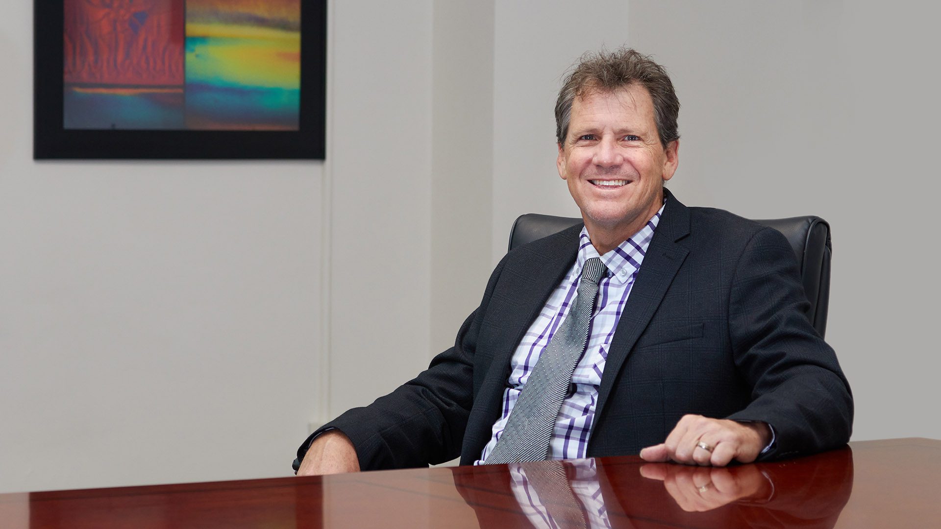 Man (Colin Gallagher) wearing a suit and tie sits at a desk