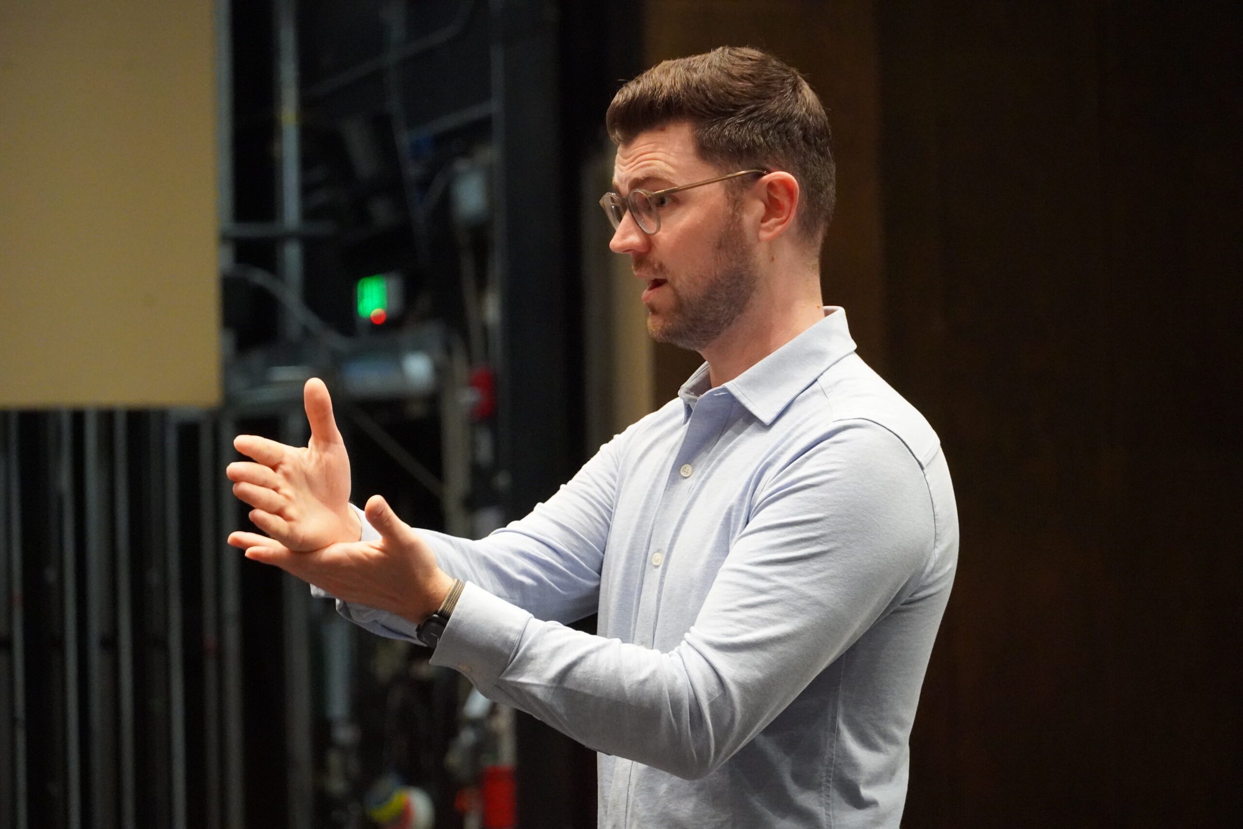 A man in a light blue dress shirt is animated as he teaches students.