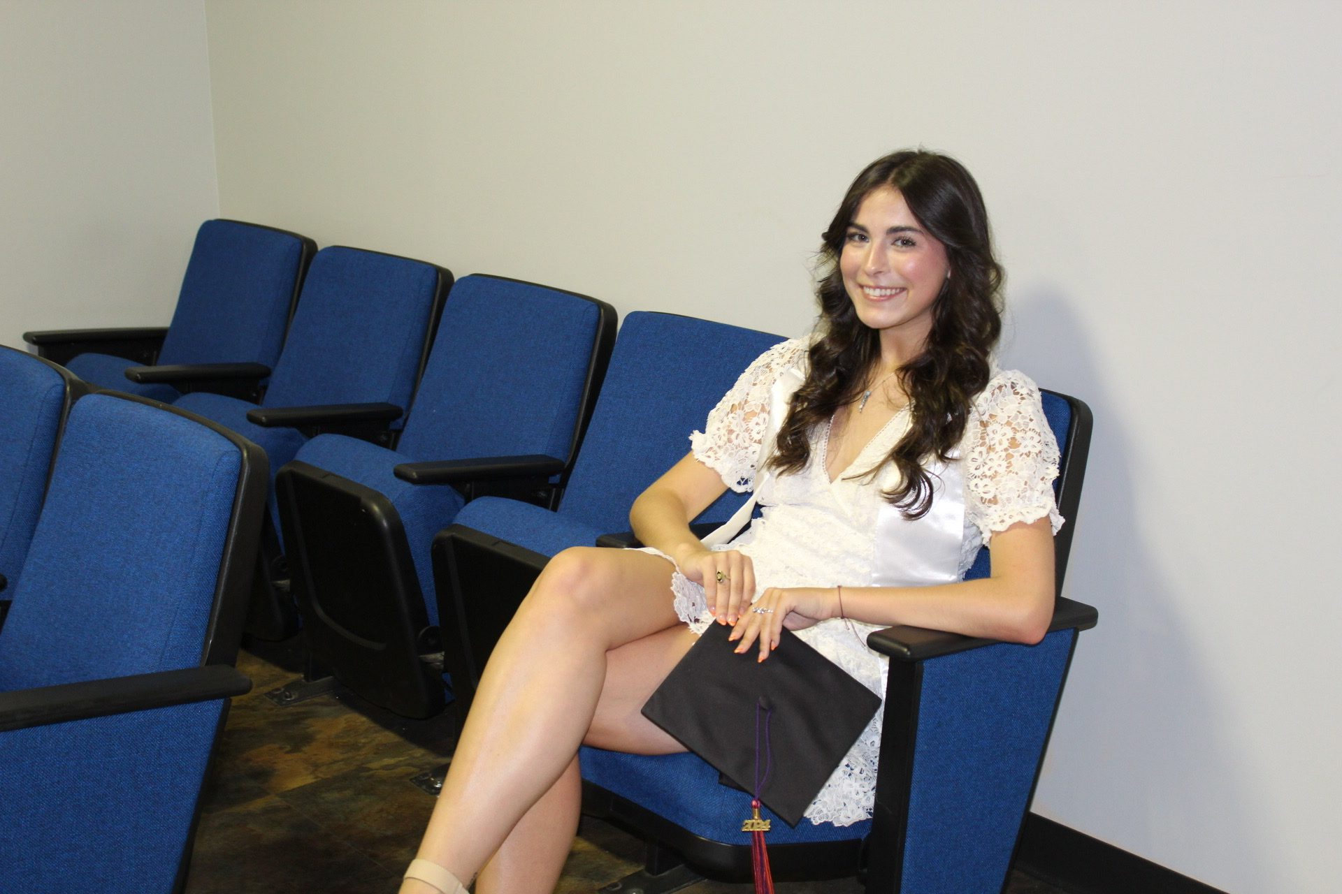 Sydney Olsen sits in McKissick Theater with a mortarboard in her hand.