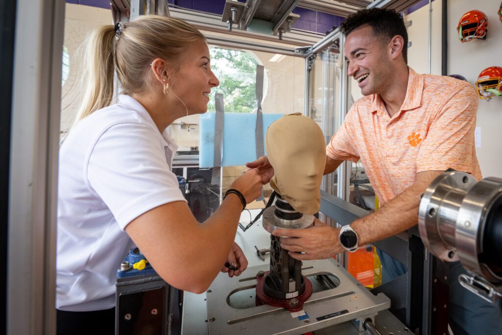 Madison and Anthony smile while positioning a fake head to a stand in the CHIP lab.