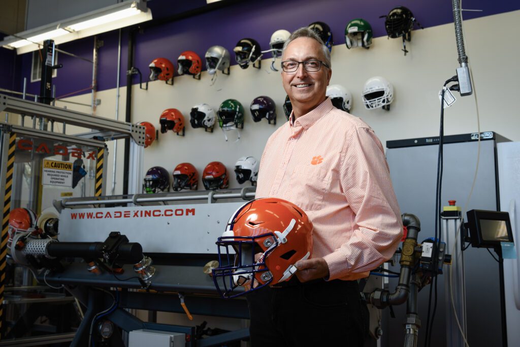 A man stands in front of a large machine holding a football helmet