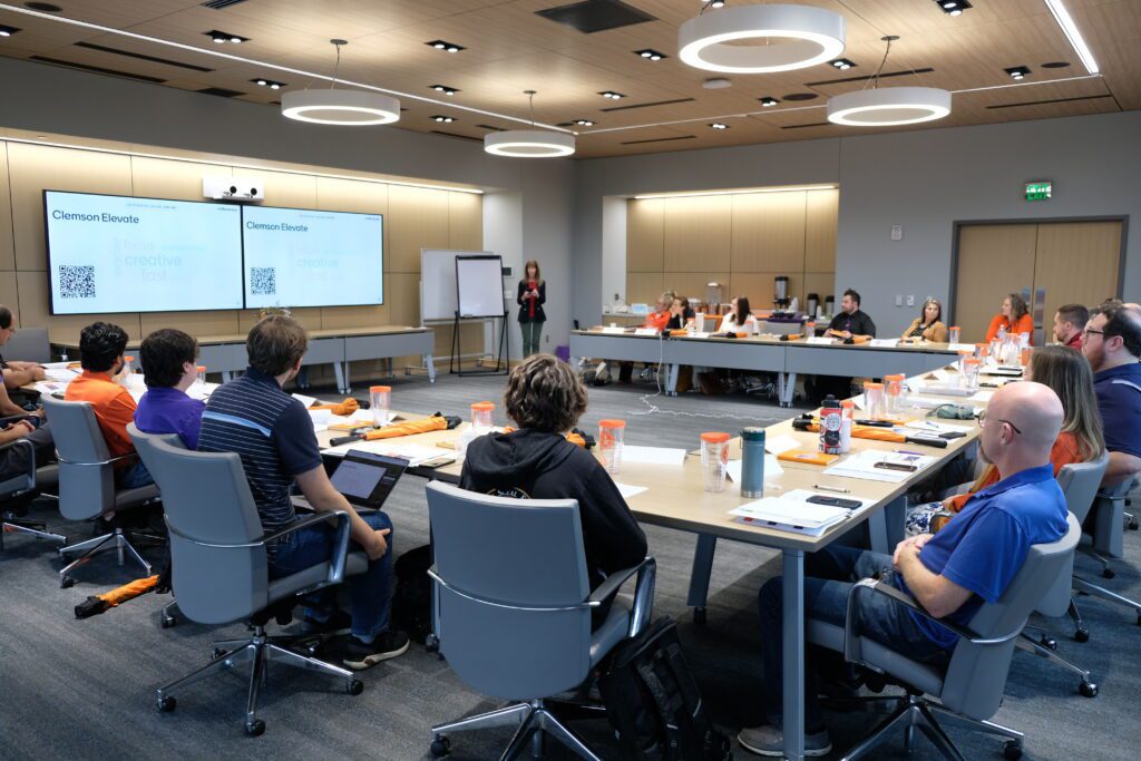 A group of CCIT employees sit around boardroom tables and listen to a speaker share more about Clemson Elevate