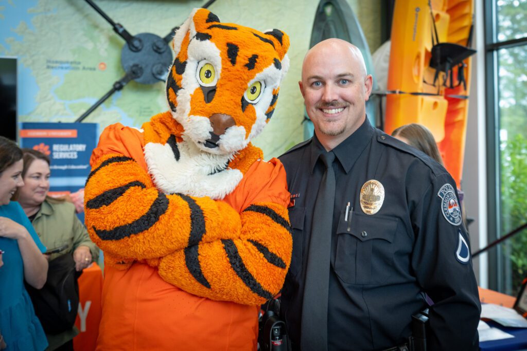 The Tiger mascot poses for a photo with his arms crossed next to a man smiling wearing a police uniform.