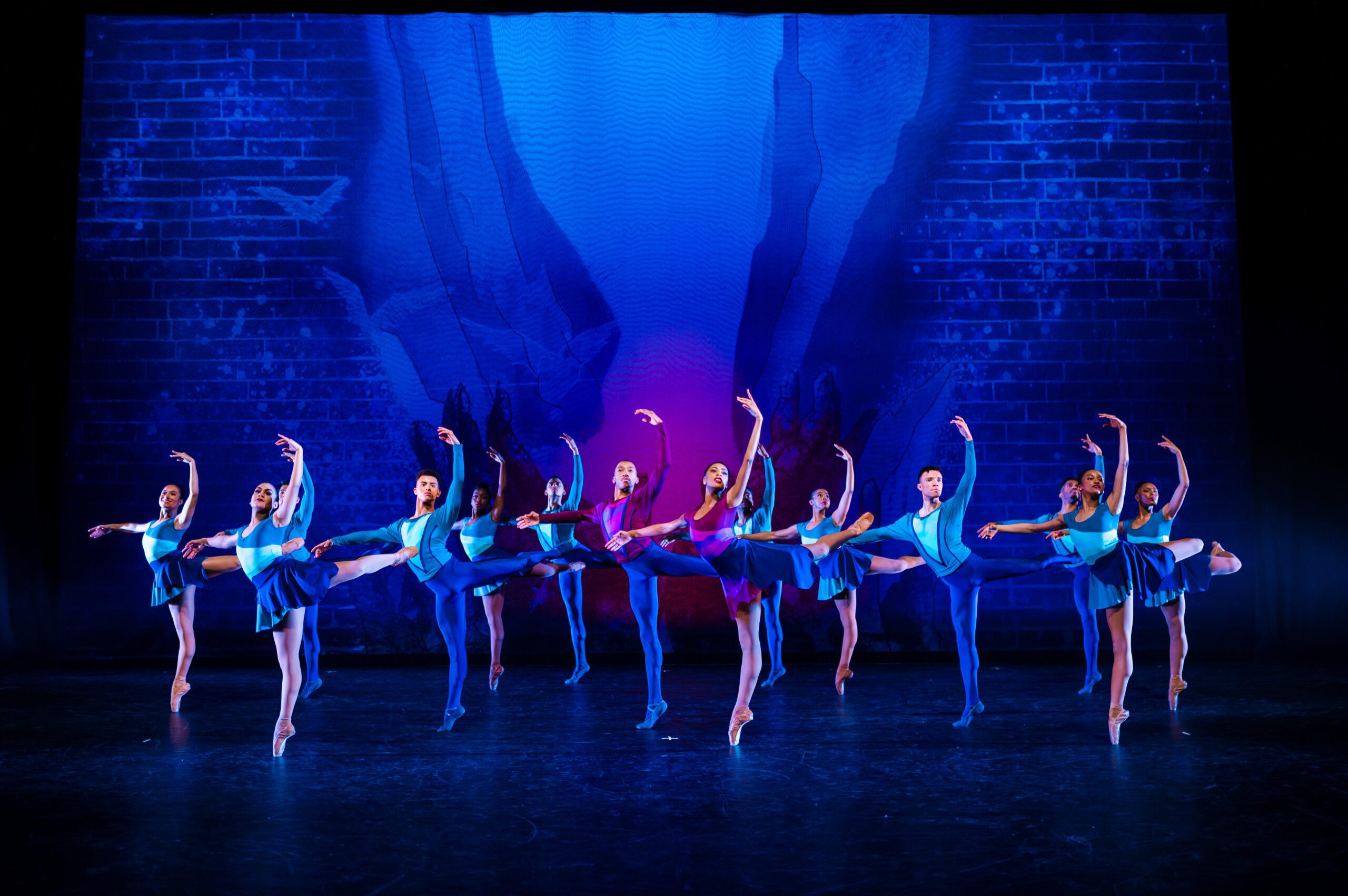 Collage Dance Collective performs on stage in front of a blue backdrop.