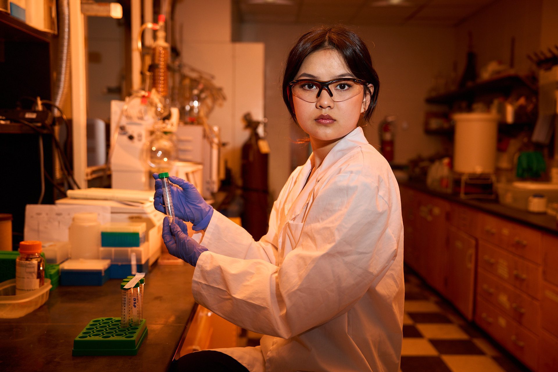 An Asian woman wearing a white lab coat holds a test tube in a lab.