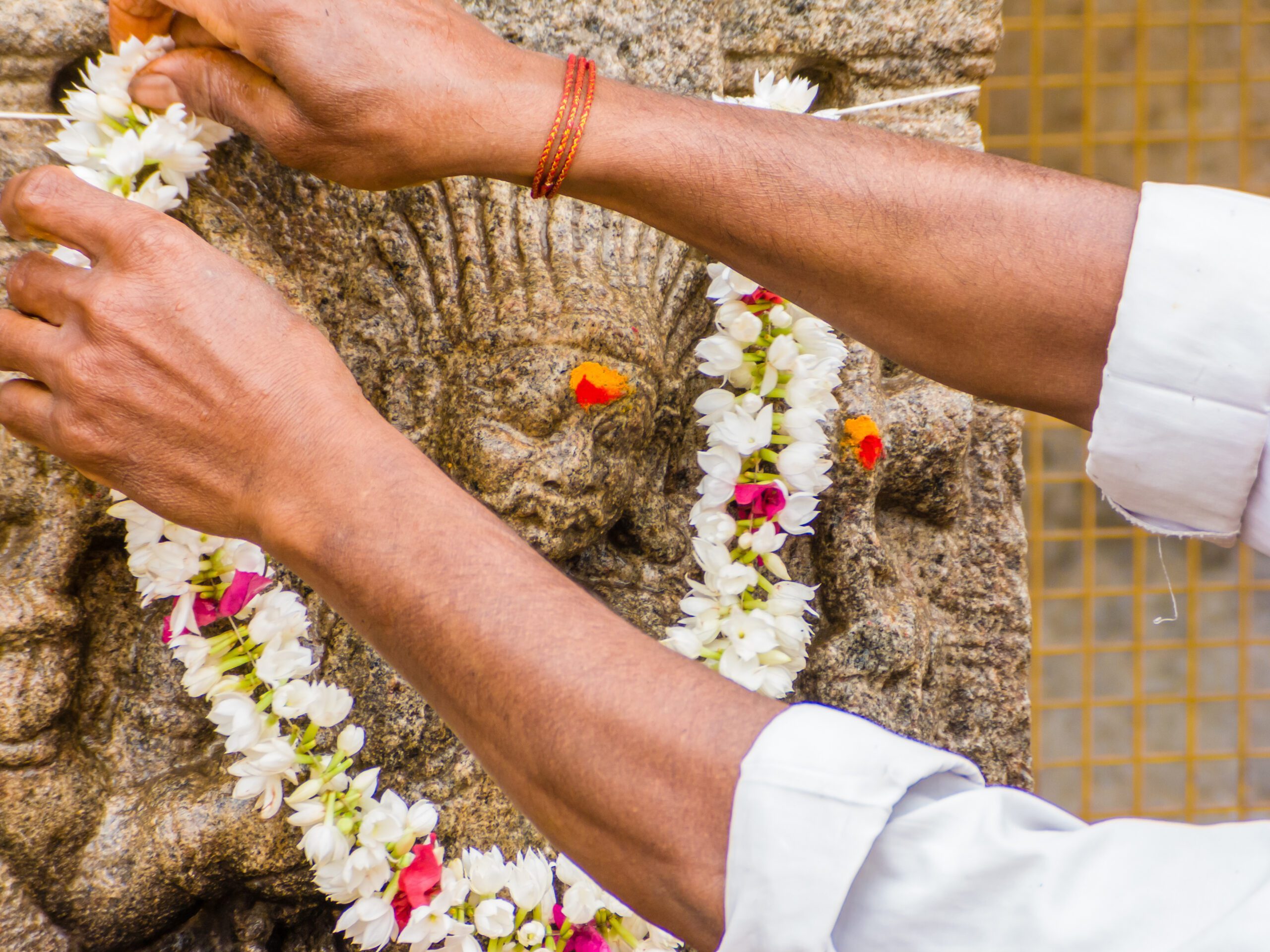 A flower wreath is placed around a stone statue by a set of hands, one with a henna tattoo.