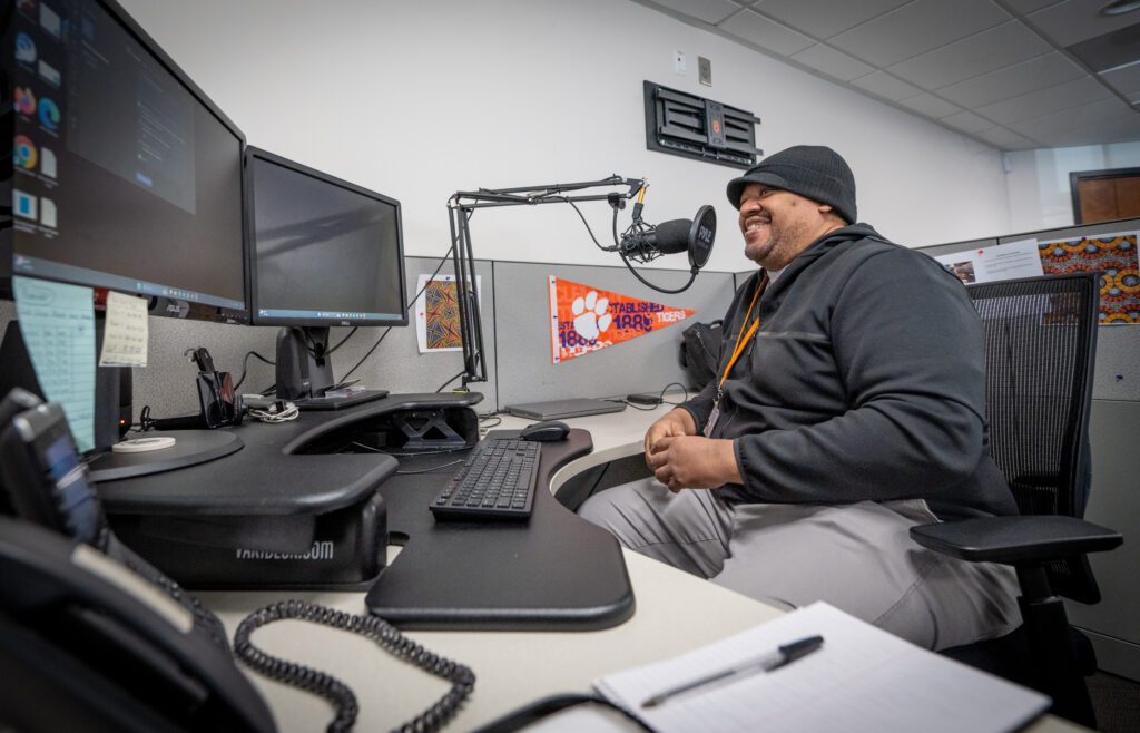 A man sits at a desk with a microphone in front of his face