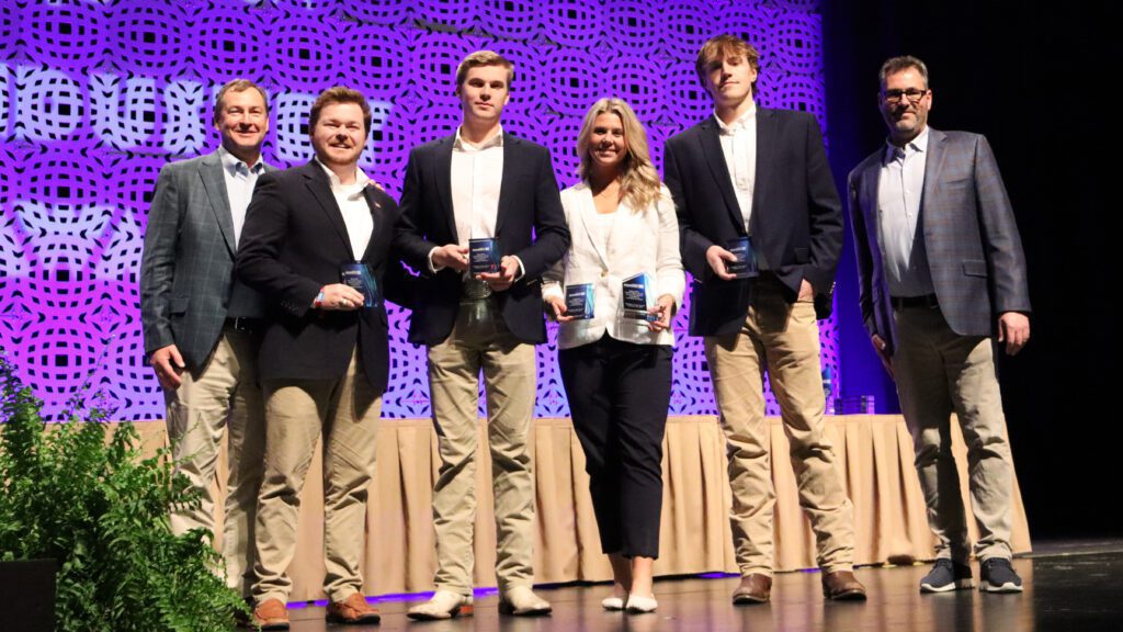 Clemson construction science and management students Samuel Davis, Tyler Brothers, Alyssa Owens and Will Hamlin hold their awards on stage with representatives from the Roofing Alliance.