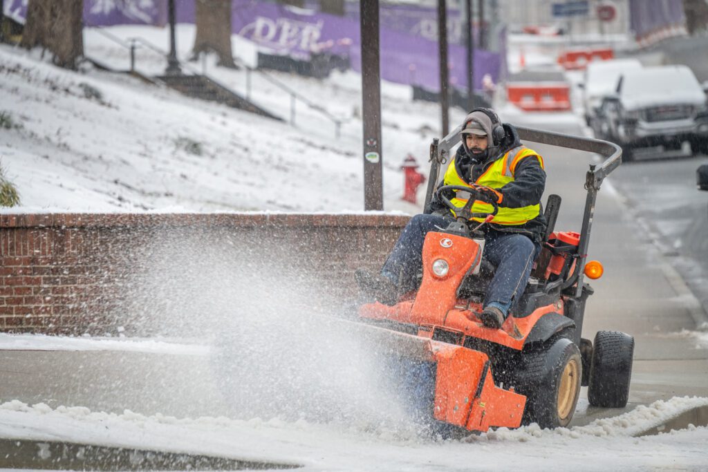 A man drives a machine that is sweeping snow off a sidewalk