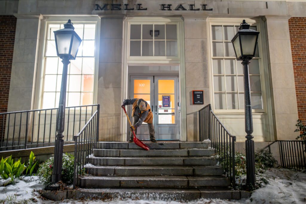 A woman shovels snow off an exterior staircase at night