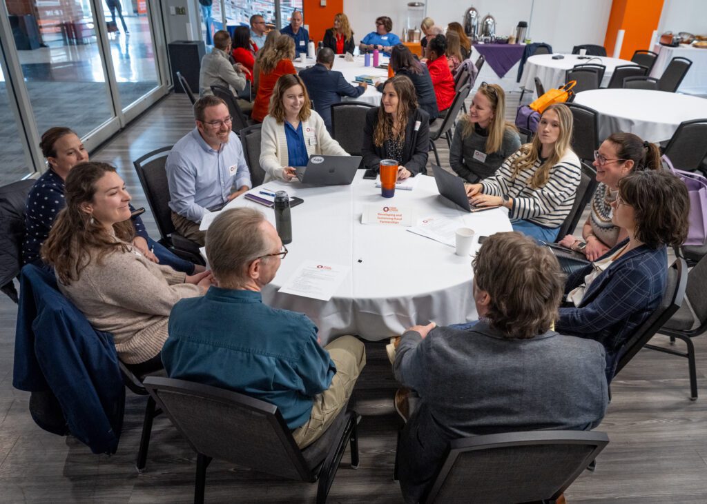A group of people sits around a round table talking