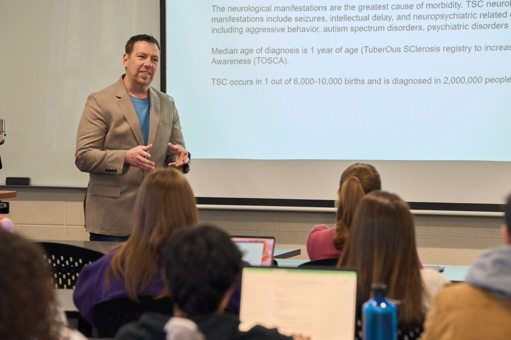 Man stands in front of a screen while teaching class.