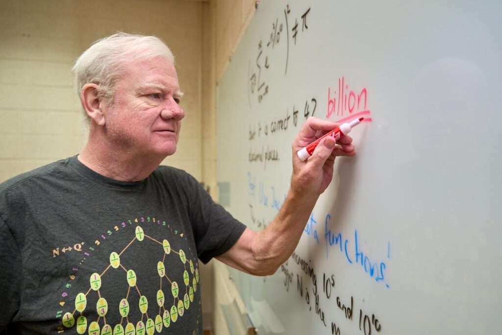 man wearing a t-shirt writes on a whiteboard