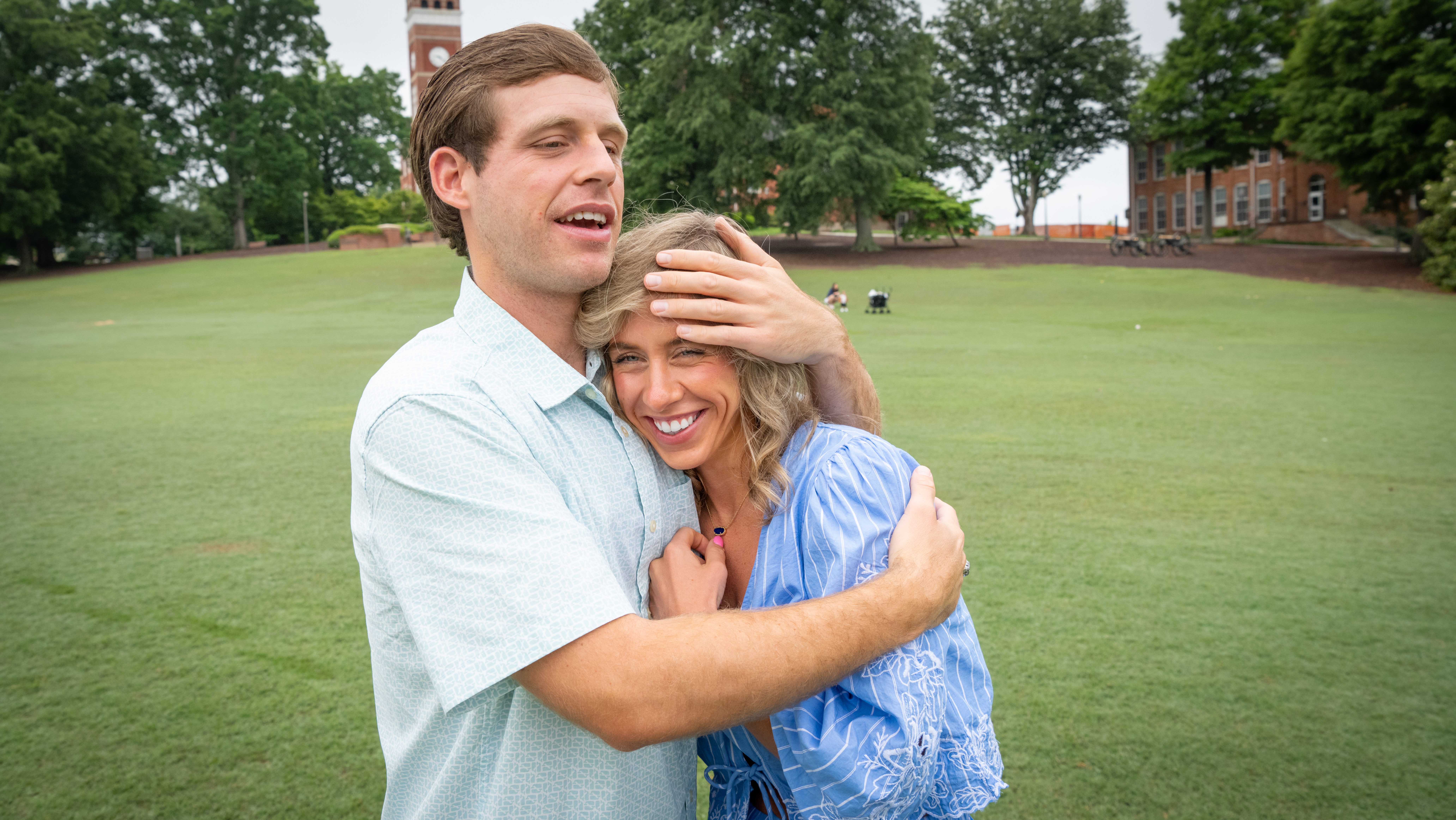 A man hugs a woman close to his chest on a grassy field