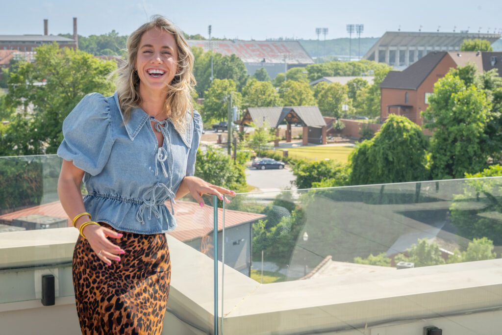A woman stands on a rooftop overlooking Memorial Stadium and laughs as the wind blows her hair