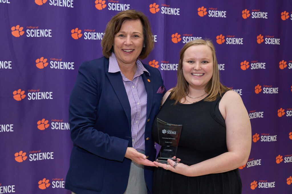 Two women stand in front of a College of Science banner holding a trophy