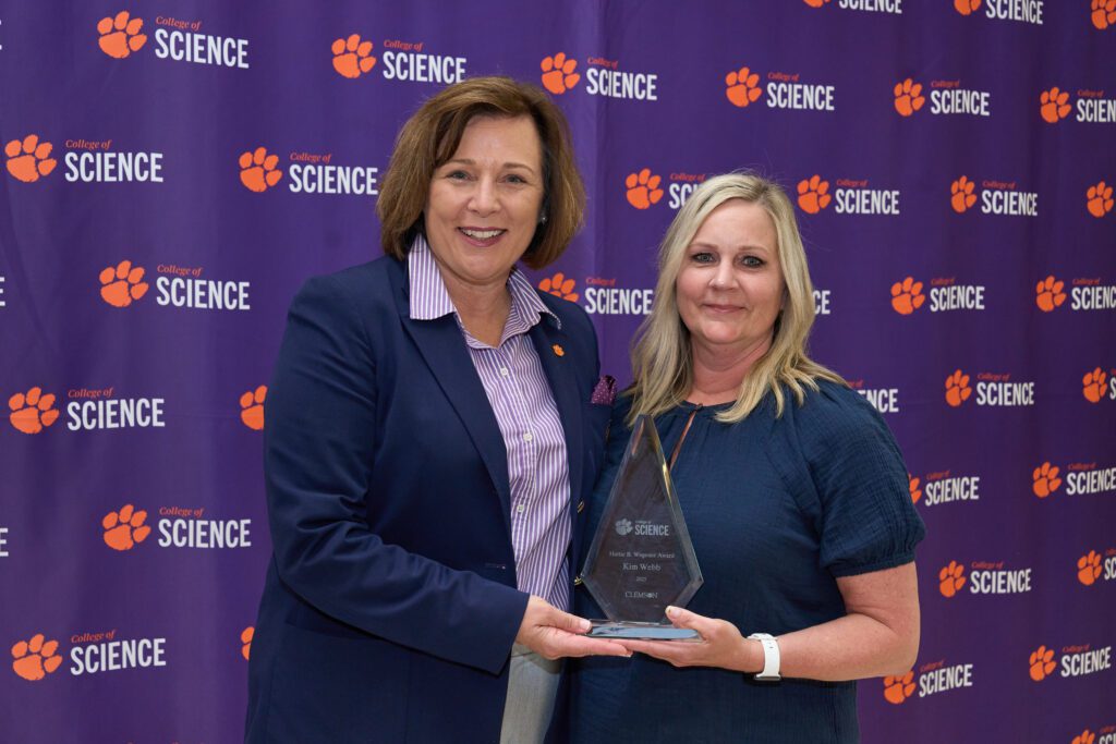 Two women stand in front of a College of Science banner and hold a trophy