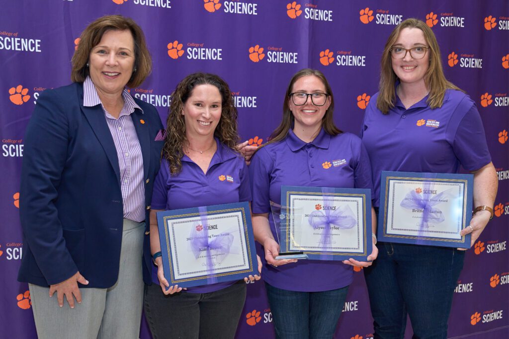 Four women stand in front of a College of Science banner, three of which are holding certificates.