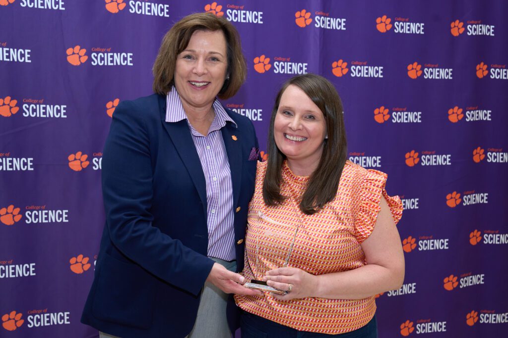 Two women stand in front of a College of Science banner holding a trophy