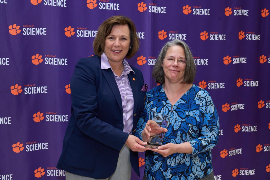 Two women stand in front of a College of Science banner holding a trophy.