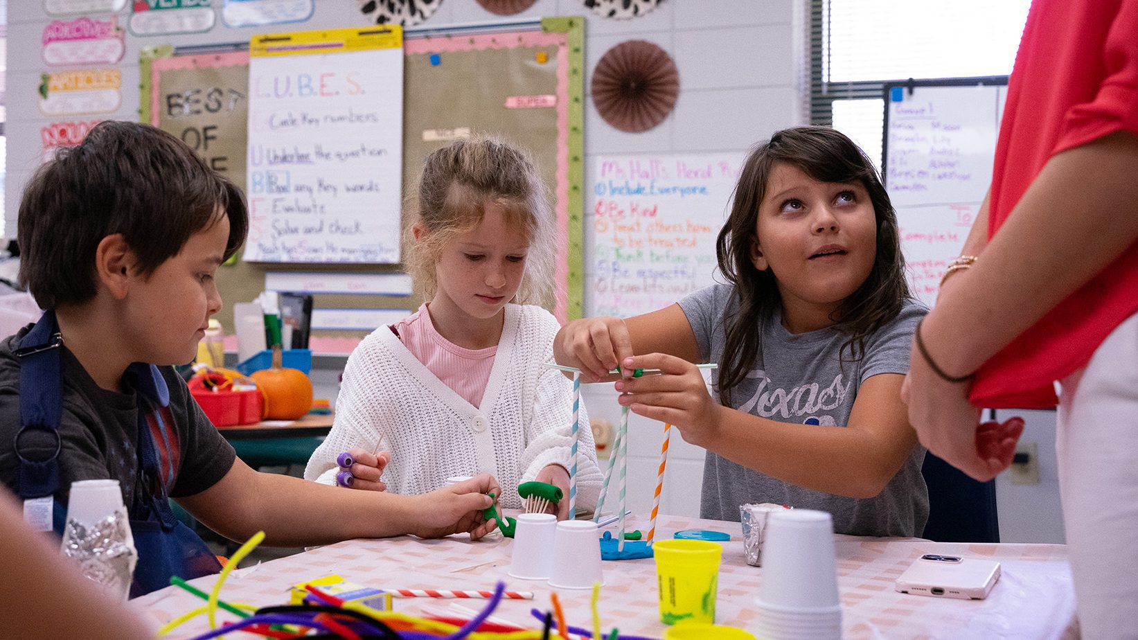 A young girl working on a science project looks up to her teacher to ask a question.