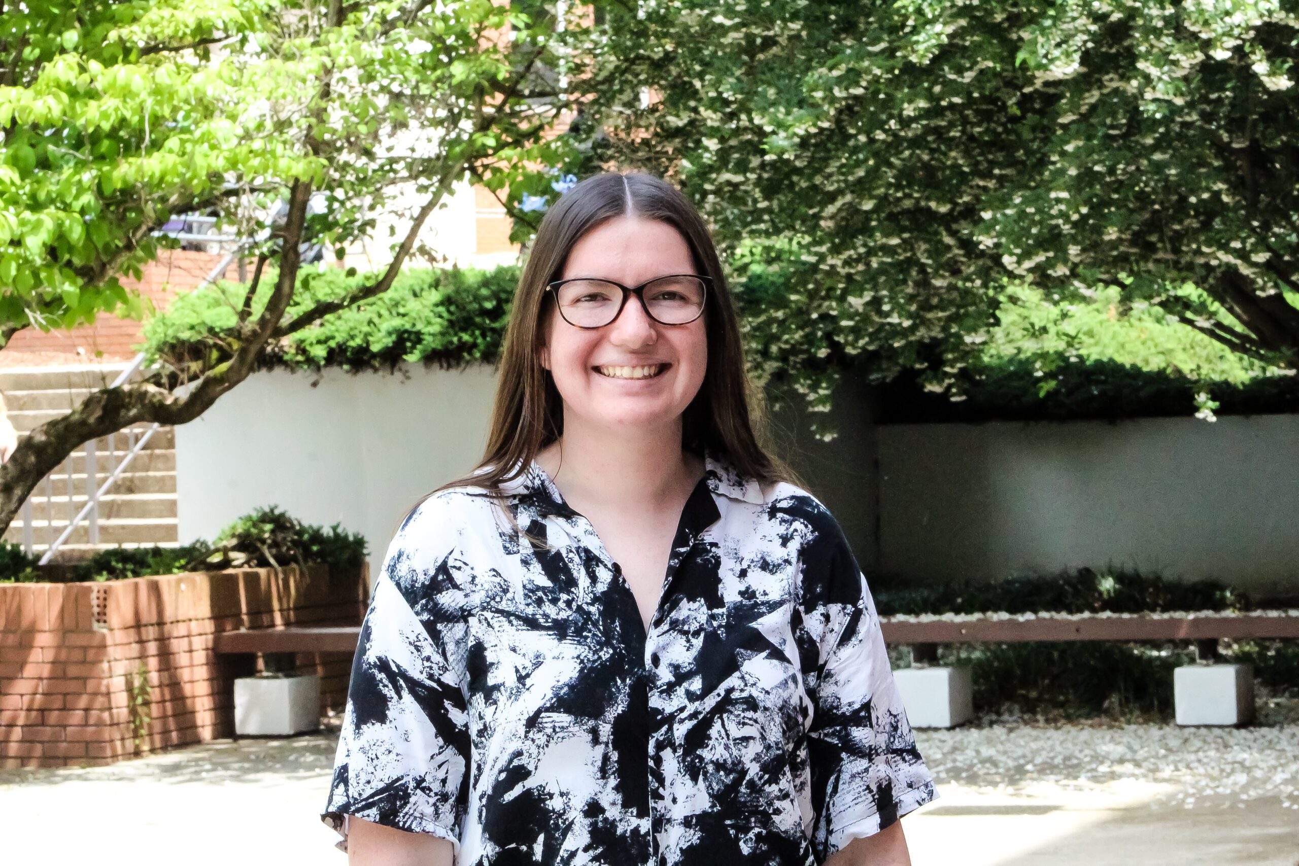 Grace Drolet, Class of 2025, stands in a courtyard with trees behind her and smiles at the camera