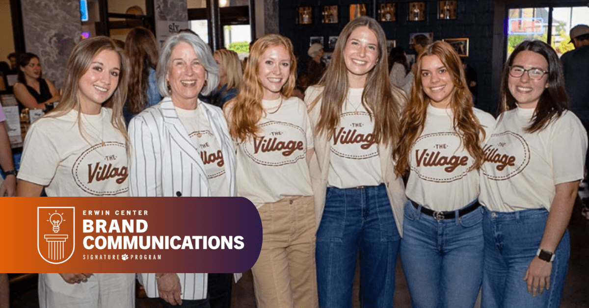 A group of five women wearing shirts with "The Village" printed on them smile for the camera.