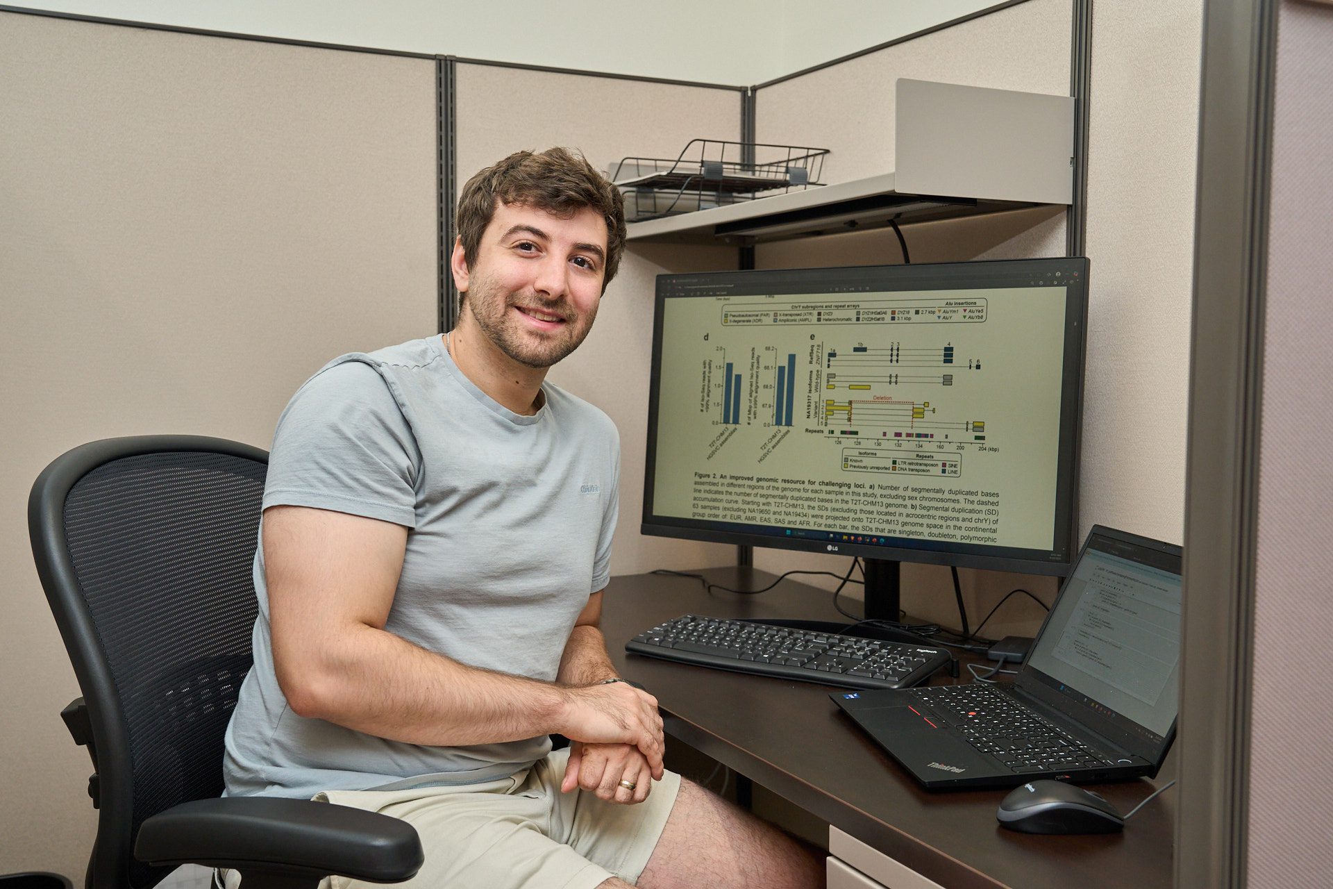 A man sitting in a chair at a computer with scientific illustrations visible on the monitor.