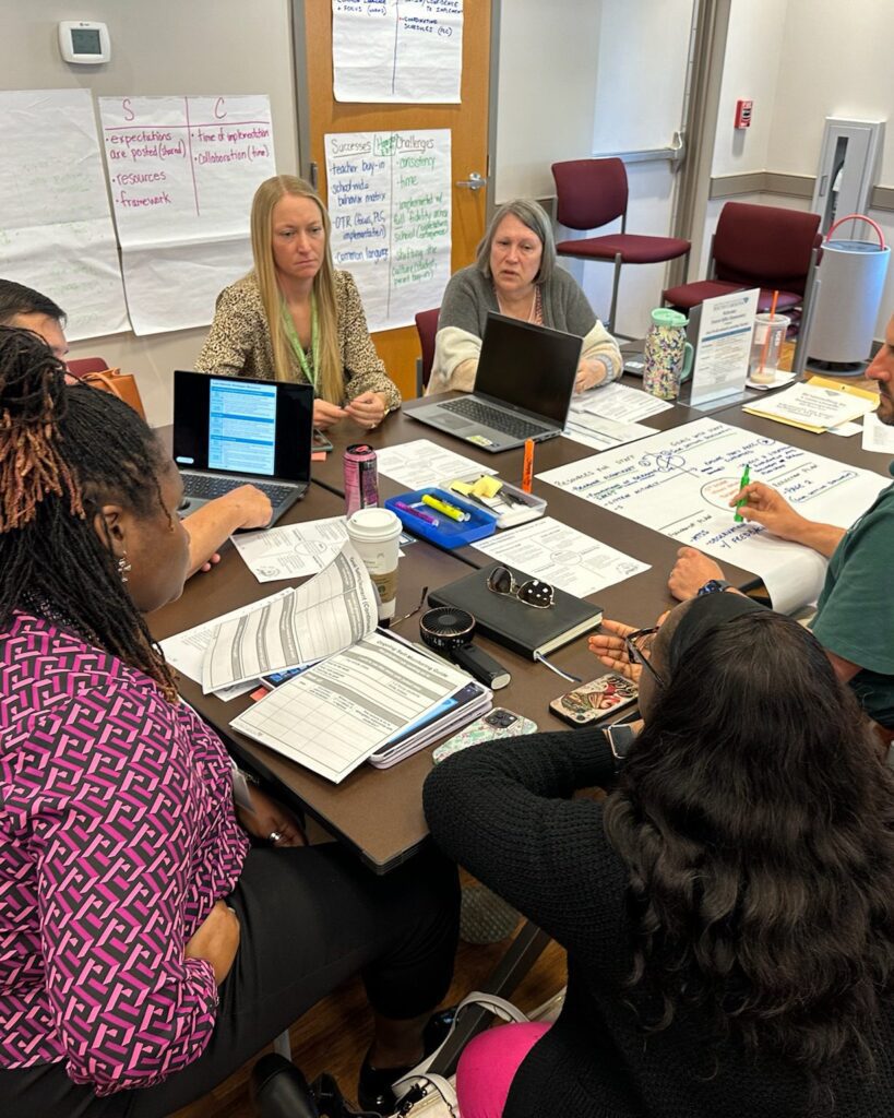 A school leadership team sits around a cluttered table to discuss approaches to student supports.