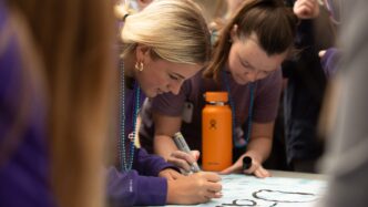 two students sign a banner at a tabling event