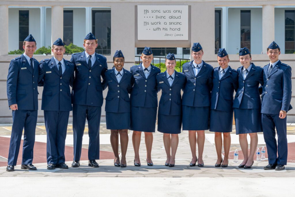 A group of ten people wearing formal Air Force dress blue uniforms stand in a line with arms around each other