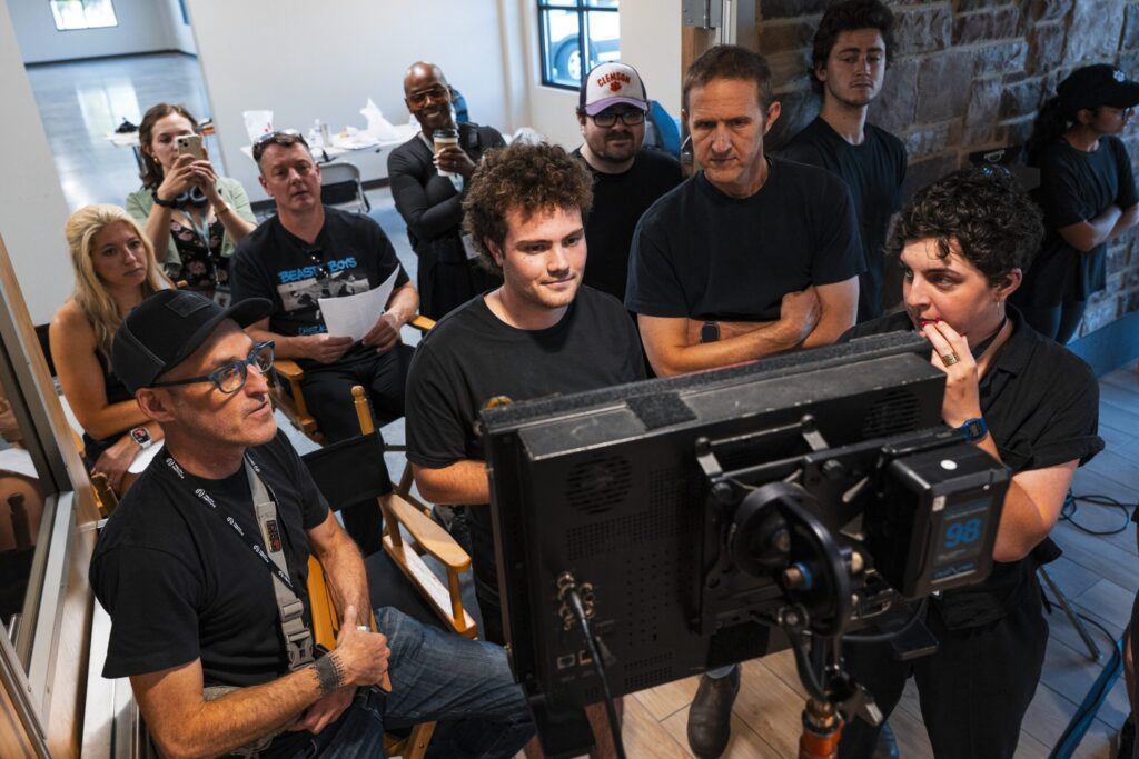 A group of World Cinema students in black t-shirts gather around a monitor to review their work