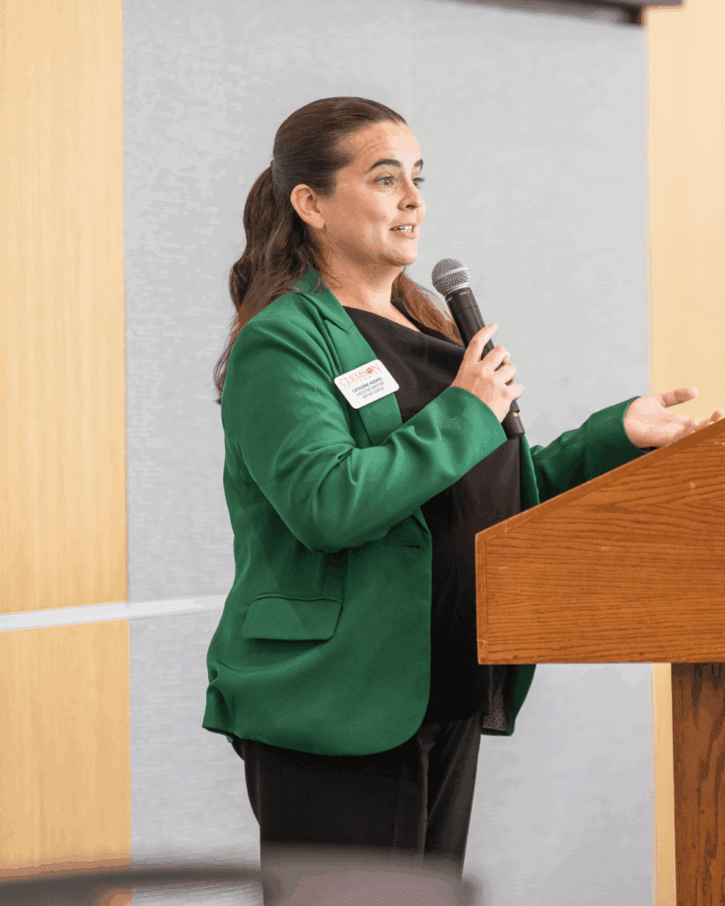 A woman in a green blazer speaks at a podium