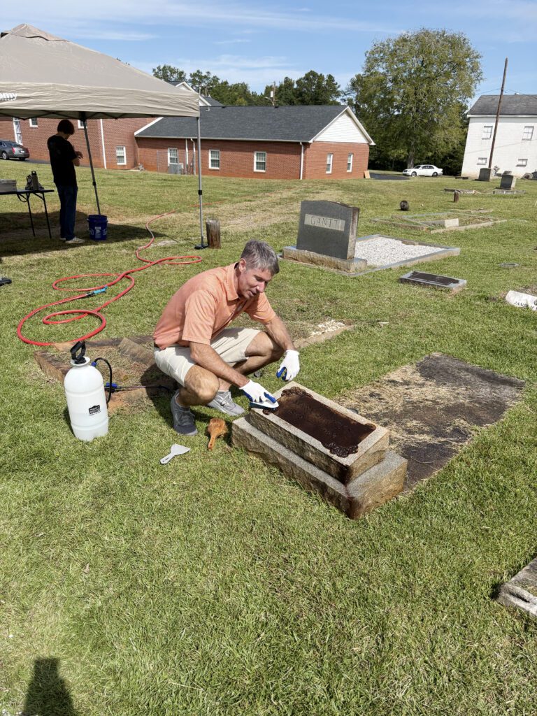 Robert Halfacre, Clemson mayor, performs community service by cleaning a grave headstone at Abel Baptist Church